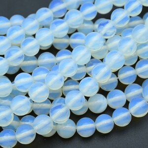 May include: A close-up of a collection of light blue opalite gemstone beads. Each round bead has a white stripe around its centre. The beads are strung together, creating a textured display. Suitable for jewellery making.