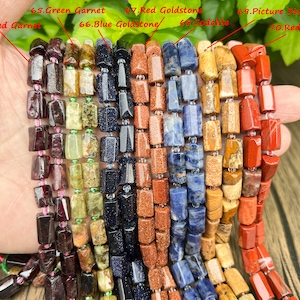 May include: Close-up of multiple strands of gemstone beads in various colors. The beads include red garnet, green garnet, blue goldstone, sodalite, picture stone, and red jasper. Each bead is rectangular and strung together.