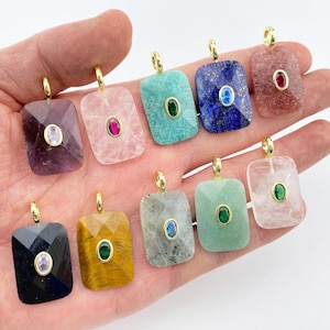 May include: A collection of rectangular gemstone pendants in various colors, including amethyst, rose quartz, and lapis lazuli. Each pendant features a smaller, contrasting gemstone in the center and a gold-colored bail.