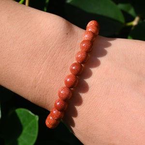 Puede incluir: Un brazalete de cuentas marrones hecho de cuentas de piedra arenisca natural. El brazalete se lleva en la mu&ntilde;eca.