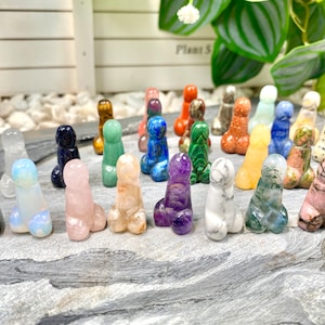 Puede incluir: Una colección de 20 pequeñas figuritas de cristal pulidas y talladas en varios colores, incluyendo negro, blanco, rosa, verde, azul, morado y marrón. Las figuritas están dispuestas sobre una superficie de piedra gris.