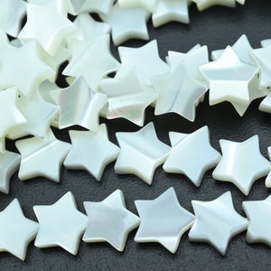 Op de afbeelding: Een verzameling witte, iriserende stervormige kralen. De kralen zijn gemaakt van parelmoer en hebben een gladde, gepolijste afwerking.