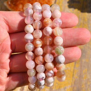 May include: Four bracelets made of pink, white, and brown agate beads. The beads are round and have a natural, polished finish.