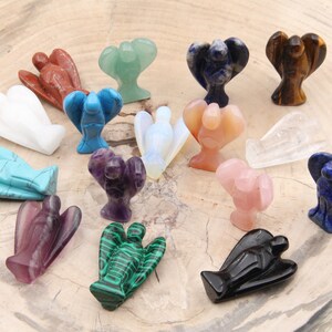 May include: A collection of 16 angel figurines carved from various gemstones, including amethyst, turquoise, rose quartz, and malachite. The figurines are arranged on a wooden surface.