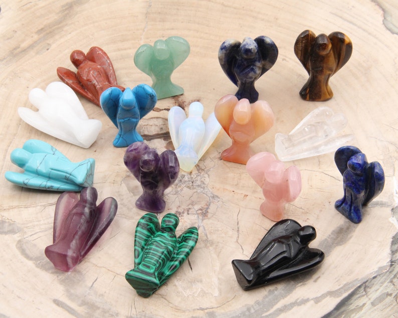 May include: A collection of 16 angel figurines carved from various gemstones, including amethyst, turquoise, rose quartz, and malachite. The figurines are arranged on a wooden surface.