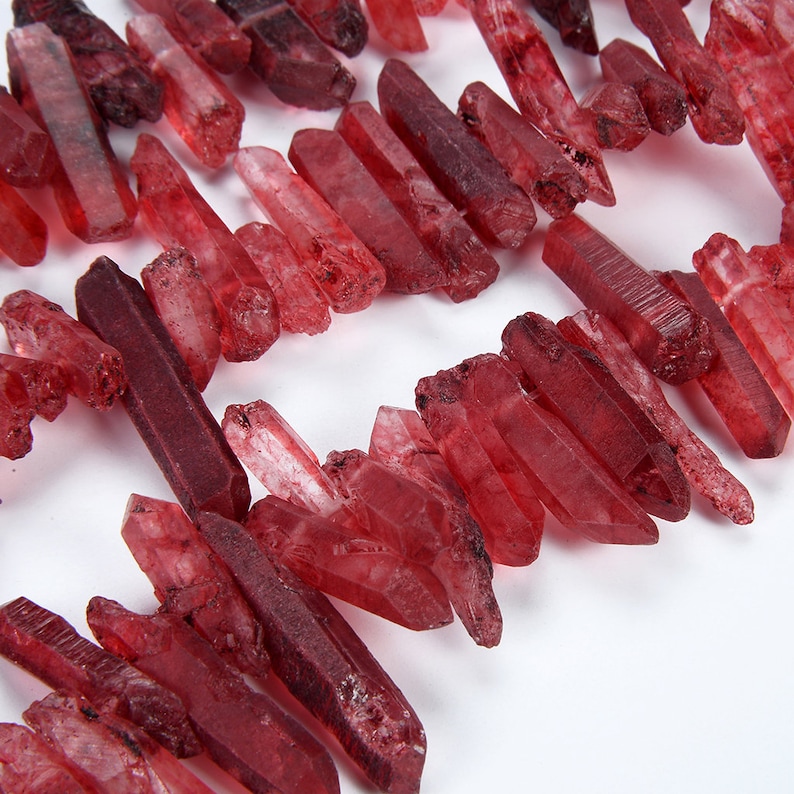 May include: A collection of red quartz crystal points, also known as red phantom quartz, arranged in a row. The crystals are various sizes and shapes, with a translucent, reddish-brown colour.