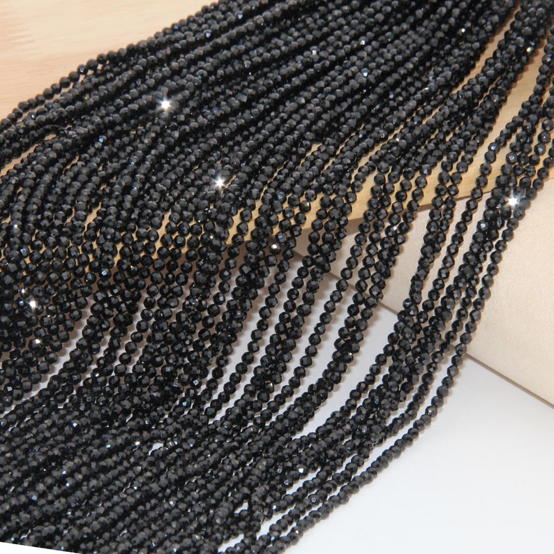 May include: A strand of black faceted beads, likely made of glass or crystal, for jewelry making. The beads are small and uniform in size, creating a sleek and elegant look.