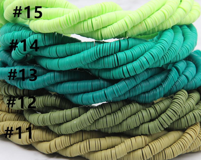 May include: A stack of five strands of colorful plastic beads. The beads are round and flat, and they are arranged in a gradient from light green to dark green. The strands are labeled with numbers 11 through 15.