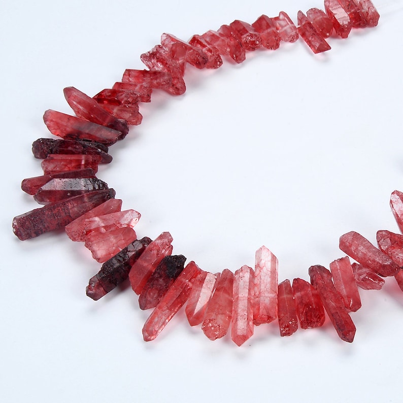 May include: A strand of red crystal points, also known as red quartz, arranged in a circle on a white background.