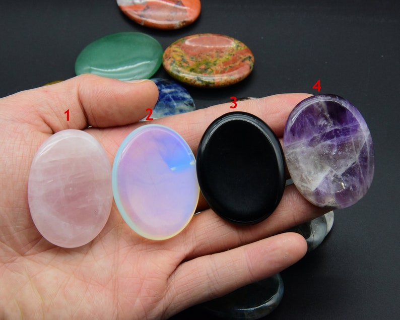 May include: Assortment of oval-shaped polished stones in various colors, including pink, white, black, purple, and green. The stones are smooth and have a natural, polished finish.