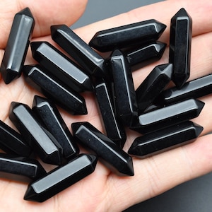 May include: A collection of black obsidian points, also known as arrowheads, are displayed on a hand. The points are smooth and polished, with a sharp tip.