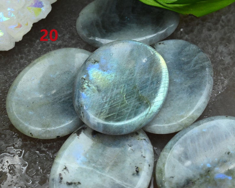 May include: A group of six oval-shaped labradorite stones, each with a smooth, polished surface. The stones are a light blue-grey color with iridescent flashes of blue, green, and gold. The stones are arranged in a semi-circle, with the text "20" visible in the upper left corner of the image.