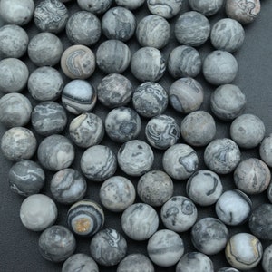 May include: A collection of round, gray gemstone beads with unique, swirling patterns in shades of gray and white. The beads have a matte finish and vary in their individual designs, creating a natural, organic look. Ideal for jewelry making.