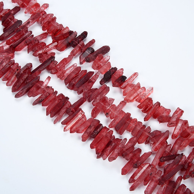 May include: A strand of red crystal quartz points, also known as red phantom quartz, arranged in a row. The points are various lengths and have a natural, raw look.