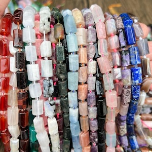 May include: Strands of colorful gemstone beads in various shapes and sizes. The beads are a mix of colors, including red, white, black, green, blue, and purple. The beads are strung together with a clear string.