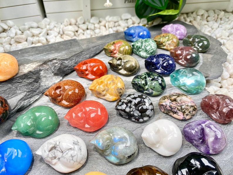May include: A collection of 20+ sleeping cat figurines carved from various types of polished stones. The cats are in various colors, including red, green, blue, white, black, and brown.