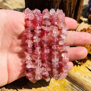 May include: A strand of pink and clear quartz chip beads. The beads are small and irregular in shape, and they are strung on a clear elastic cord.