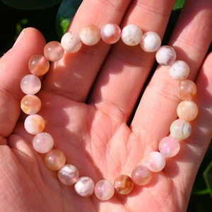 May include: A pink and white agate gemstone bracelet with round beads. The bracelet is made of natural stones and has a polished finish.