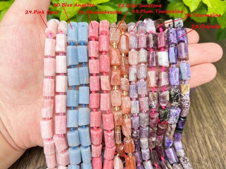 May include: Strands of gemstone beads in various colors, including pink, blue, and purple. The beads are rectangular and strung together with pink or blue string. The gemstones are labeled: Pink Opal, Blue Angelite, Rhodochrosite, Gold Sunstone, Plum Tourmaline, Tourmaline, and Charoite.