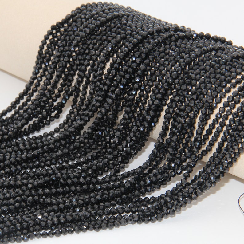 May include: A strand of black faceted gemstone beads. The beads are small and round, and they are strung together on a clear thread. The beads are arranged in a loose, flowing pattern.