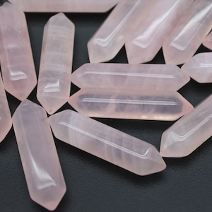 May include: A group of pink rose quartz crystal points, also known as rose quartz wands, are arranged on a black surface. The points are smooth and polished, with a light pink color.