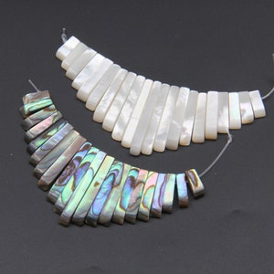 May include: Two strands of iridescent shell beads, one white and one with a rainbow of colors. The beads are rectangular and arranged in a fan shape.