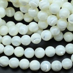 Puede incluir: Una hebra de cuentas redondas blancas hechas de madreperla. Las cuentas tienen un brillo iridiscente sutil.