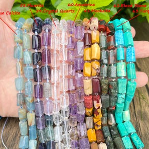 May include: A selection of gemstone bead strands, including blue calcite, fluorite, crystal quartz, amethyst, mookaite, bloodstone, and turquoise. The beads are rectangular and strung together, showcasing a variety of colors and textures.