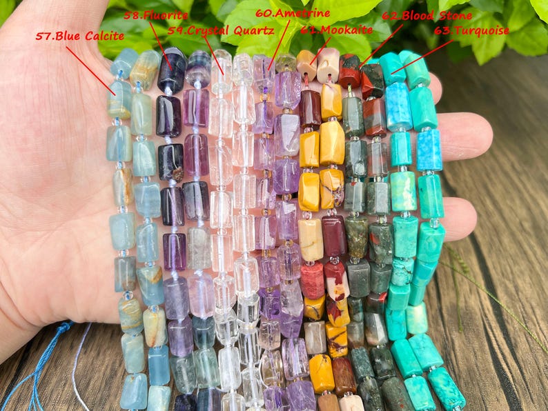 May include: A selection of gemstone bead strands, including blue calcite, fluorite, crystal quartz, amethyst, mookaite, bloodstone, and turquoise. The beads are rectangular and strung together, showcasing a variety of colors and textures.