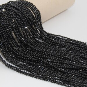 May include: A strand of black faceted gemstone beads. The beads are small and round, and they are strung together on a clear thread. The beads are arranged in a loose, flowing pattern.