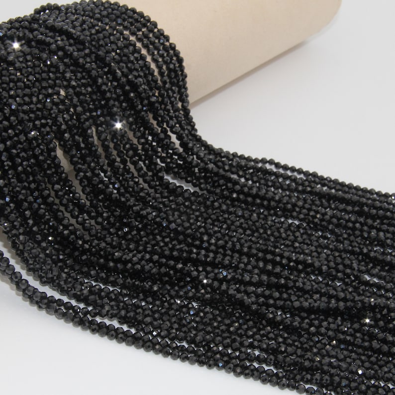 May include: A strand of black faceted gemstone beads. The beads are small and round, and they are strung together on a clear thread. The beads are arranged in a loose, flowing pattern.