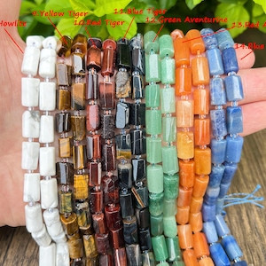 May include: A hand holds multiple strands of rectangular gemstone beads. The beads are in various colors, including white, yellow, red, green, orange, and blue. The gemstones are labeled as Howlite, Yellow Tiger, Red Tiger, Blue Tiger, Green Aventurine, Red Aventurine, and Blue Aventurine.