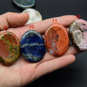 May include: Assortment of 10 oval-shaped polished stones, each with a unique pattern and color. The stones are arranged in a row on a hand, with the numbers 9, 10, 11, and 12 visible.