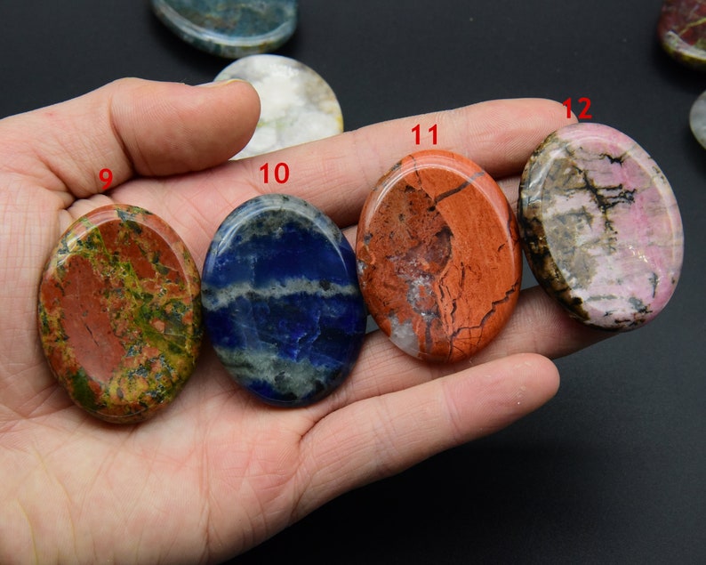 May include: Assortment of 10 oval-shaped polished stones, each with a unique pattern and color. The stones are arranged in a row on a hand, with the numbers 9, 10, 11, and 12 visible.