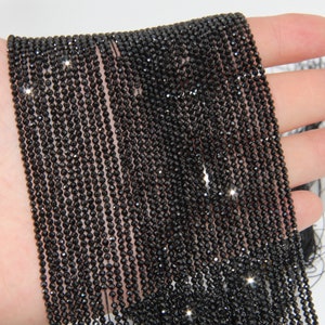 May include: A strand of black faceted gemstone beads. The beads are small and round, and they have a shiny, polished finish.