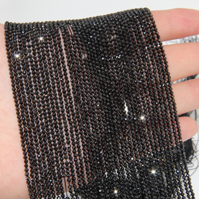 May include: A strand of black faceted gemstone beads. The beads are small and round, and they have a shiny, polished finish.