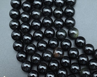 May include: Close-up of a collection of glossy, black obsidian gemstone beads. The spherical beads reflect light, creating a shiny appearance. The beads are arranged closely together, suggesting they are part of a necklace or bracelet. The beads are approximately 1 cm in diameter.