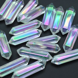 Pode incluir: Um grupo de pontas de cristal de vidro transparente iridescente, também conhecidas como varinhas, com um efeito arco-íris. As pontas estão dispostas em um padrão aleatório sobre uma superfície preta.