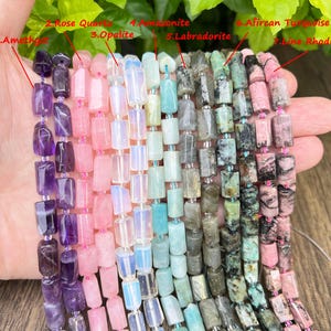 May include: A hand displays strands of gemstone beads in various colors. The gemstones include amethyst, rose quartz, opalite, amazonite, labradorite, African turquoise, and line rhodonite. Each bead is rectangular and strung together.
