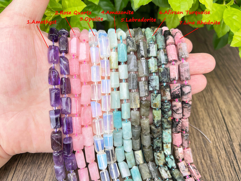 May include: A hand displays strands of gemstone beads in various colors. The gemstones include amethyst, rose quartz, opalite, amazonite, labradorite, African turquoise, and line rhodonite. Each bead is rectangular and strung together.