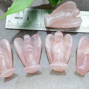 Puede incluir: Cuatro figuras de &aacute;ngeles de cuarzo rosa. Los &aacute;ngeles est&aacute;n tallados con alas detalladas y t&uacute;nicas fluidas. Una regla muestra que los &aacute;ngeles miden aproximadamente 2,5 cm de altura. Los &aacute;ngeles se exhiben sobre una superficie gris claro.