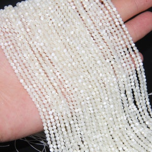 May include: A strand of white iridescent shell beads. The beads are small and round, with a slightly faceted surface. The beads are strung on a thin white thread.