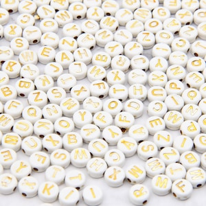 May include: White round beads with gold letters of the alphabet. The beads are for crafting and jewelry making.