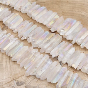 May include: A collection of white iridescent quartz crystal points, also known as angel aura quartz, arranged in rows on a wooden surface.