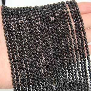 May include: A strand of black faceted gemstone beads. The beads are small and round, and they have a shiny, polished finish.