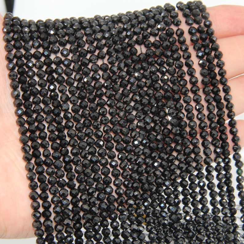 May include: A strand of black faceted gemstone beads. The beads are small and round, and they have a shiny, polished finish.