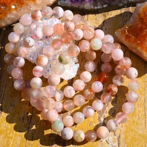May include: A strand of pink, white, and green agate beads. The beads are round and have a natural, polished finish. The beads are strung on a clear elastic cord.