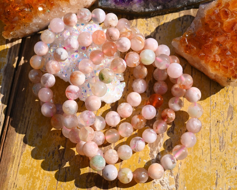May include: A strand of pink, white, and green agate beads. The beads are round and have a natural, polished finish. The beads are strung on a clear elastic cord.