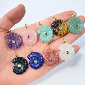 May include: A collection of gemstone pendants in various colors, including amethyst, rose quartz, and jade. Each pendant is carved in a spiral seashell design and features a small gemstone accent and a gold-colored bail.