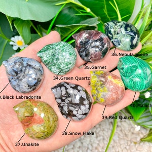 May include: A collection of ten small, polished, carved stone animal figurines. The figurines are in various colors and patterns, including green, red, black, white, and gray. The stones are labeled with their names, including Green Quartz, Black Labradorite, Snow Flake, Red Quartz, Malachite, Garnet, Nebula Stone, and Unakite.